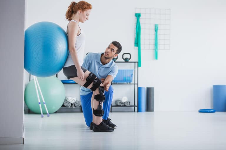 Woman With Orthopedic Problem Exercising With Ball While Physiot